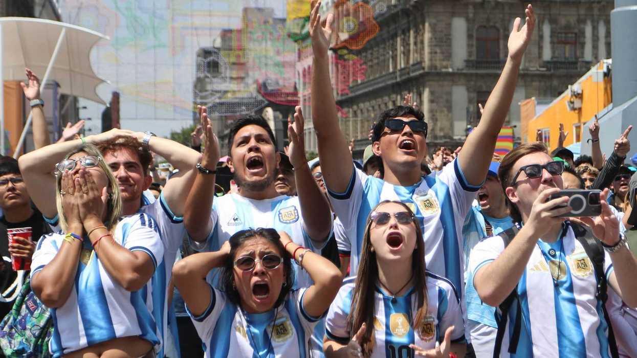 Excited fans in Argentina jerseys cheer in a lively outdoor setting.