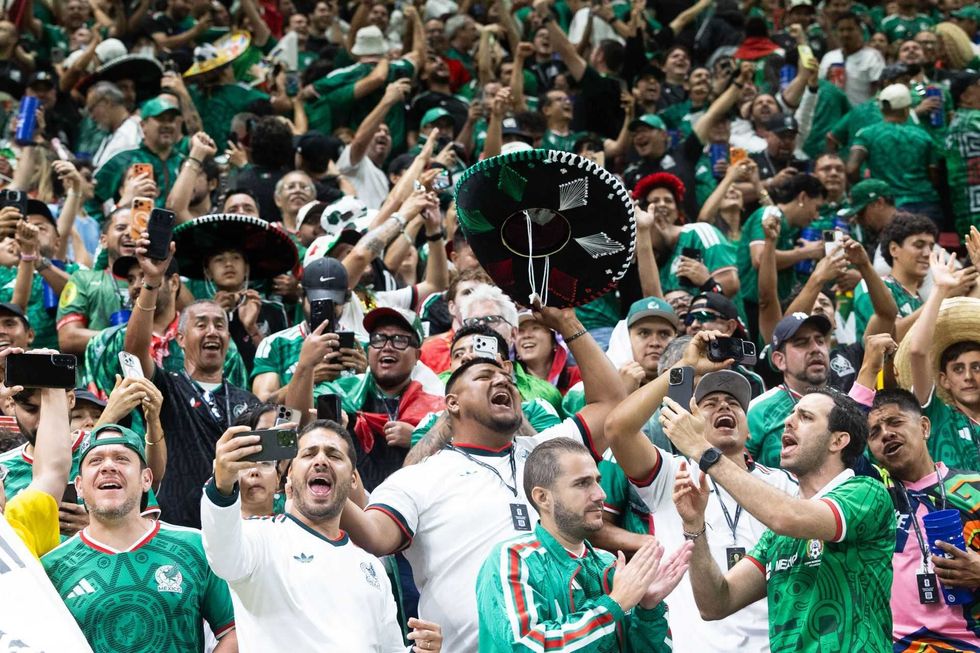 Excited soccer fans in green jerseys cheer with phones and sombreros in the stadium.