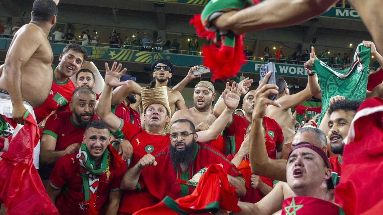 Excited soccer fans in red, cheering and waving flags in a stadium.