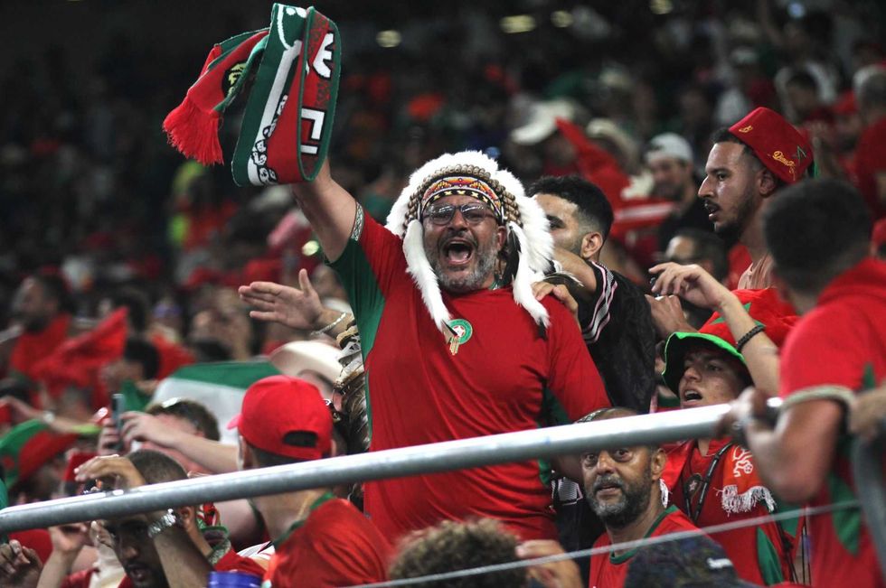 Excited soccer fans in red shirts cheering at a stadium match.