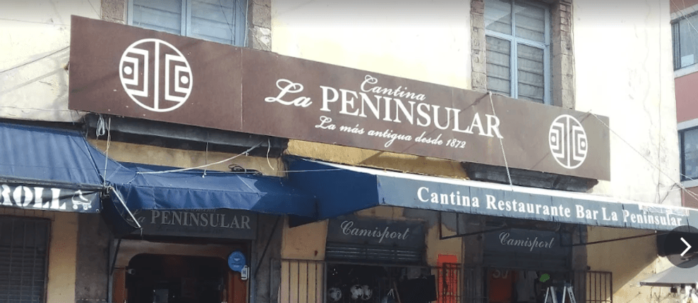 Exterior of Cantina La Peninsular with blue awnings and brown sign.