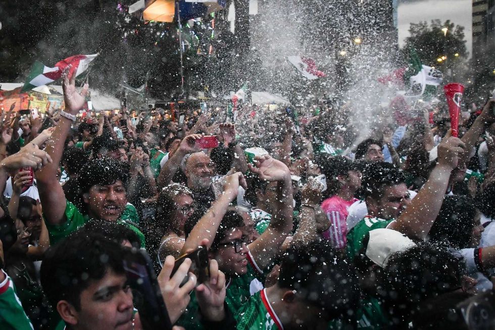 Fans celebrating energetically with flags and confetti in a crowded outdoor gathering.