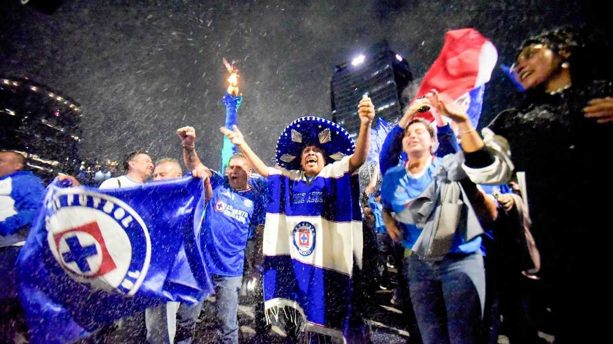 Fans celebrating with flags and fireworks in the rain at night.