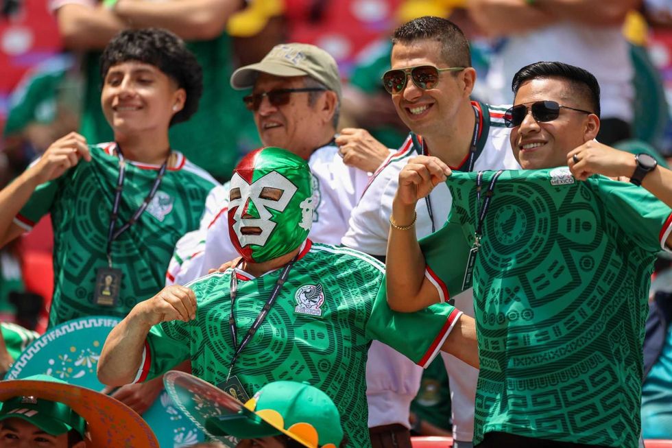 Fans in green jerseys and a lucha libre mask celebrate at a stadium.