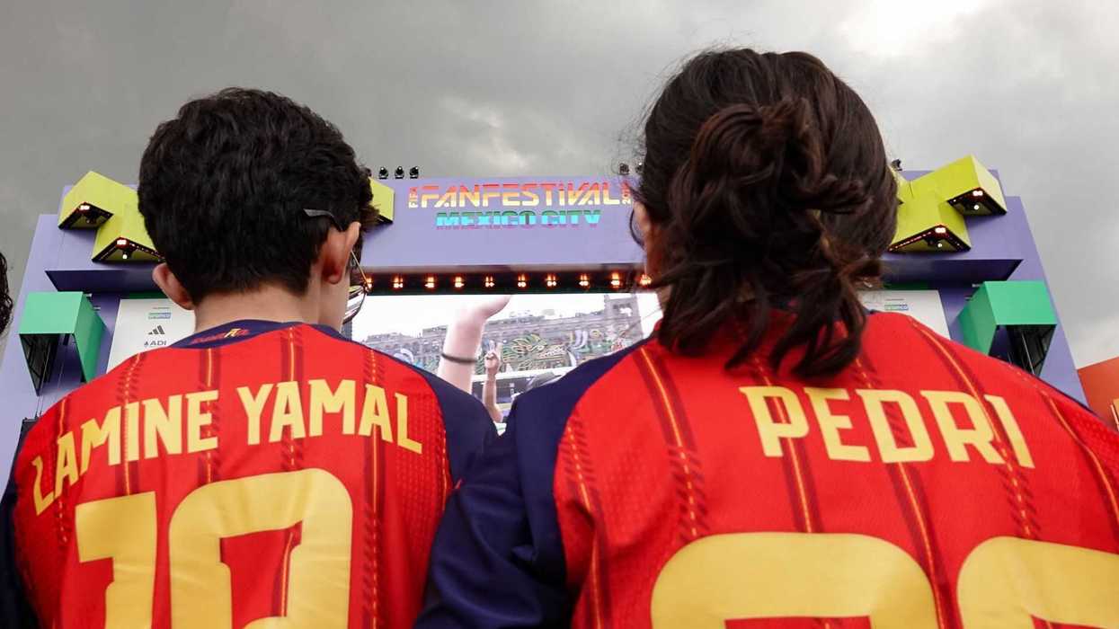 Fans in jerseys watch a match on a large screen at a fan festival.