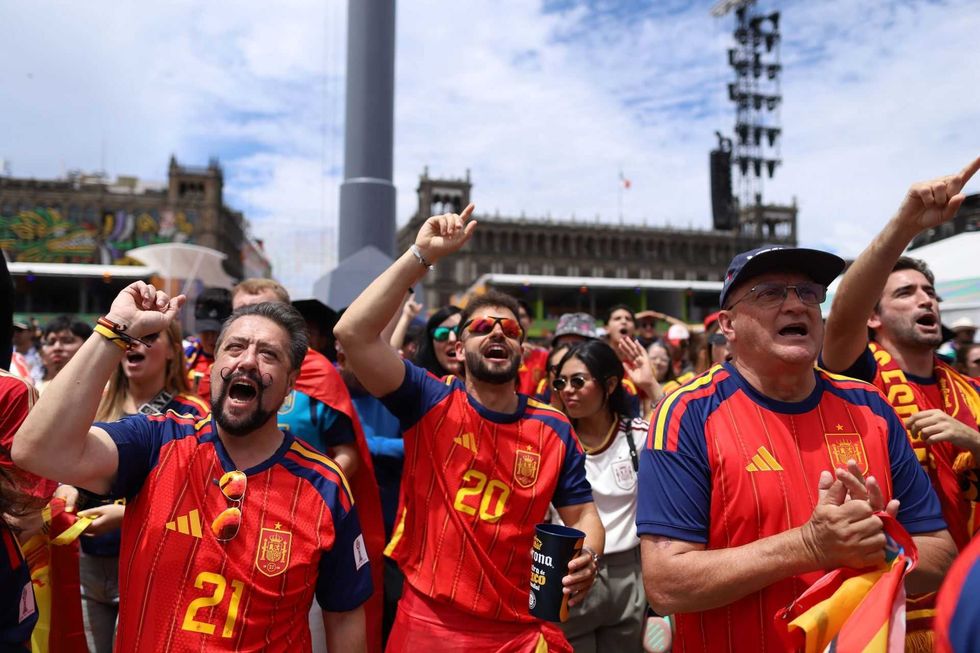 Fans in red Spain jerseys cheer energetically at an outdoor sports event.