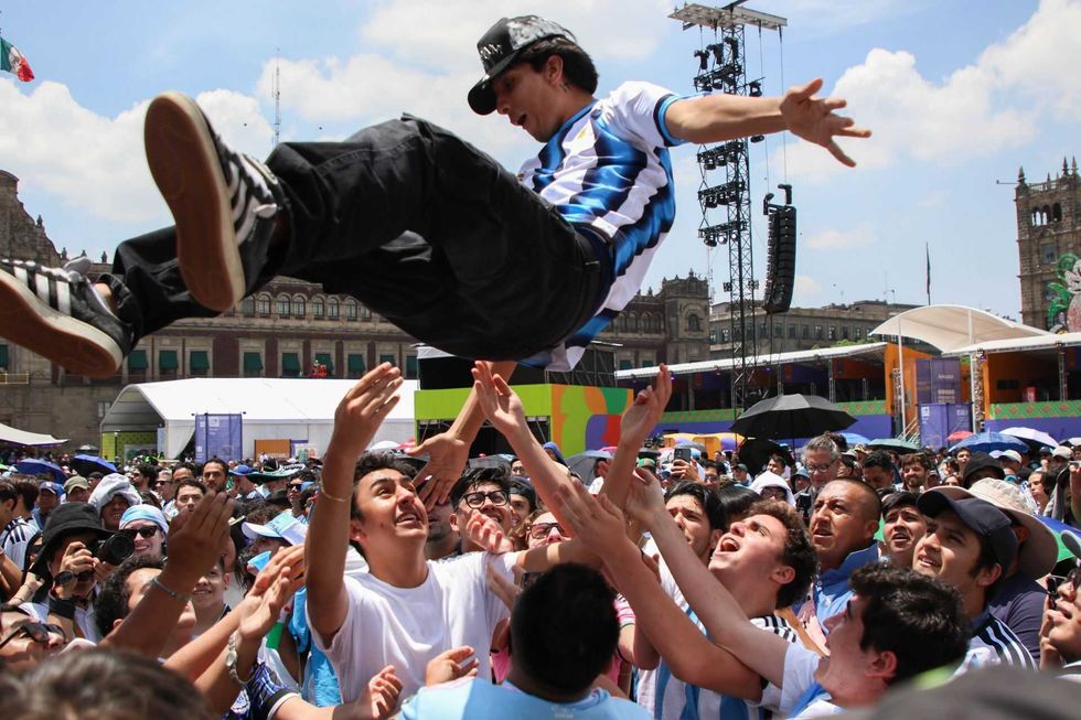 Fans lift a person in an Argentine jersey at an outdoor event.