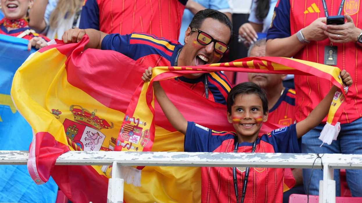 Fans wearing Spain jerseys, joyfully waving Spanish flag at a sports event.