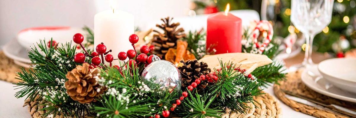 Festive table centerpiece with candles, pinecones, and Christmas tree in the background.