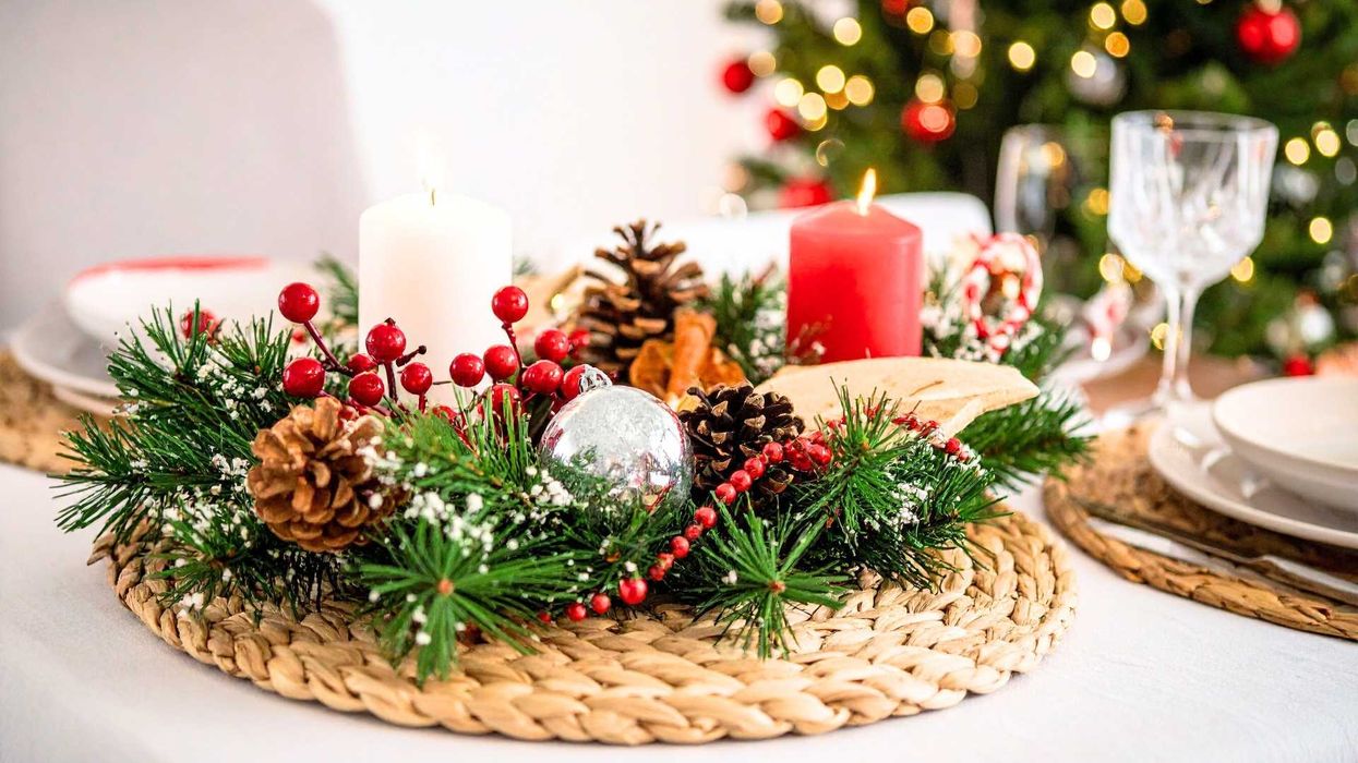 Festive table centerpiece with candles, pinecones, and Christmas tree in the background.