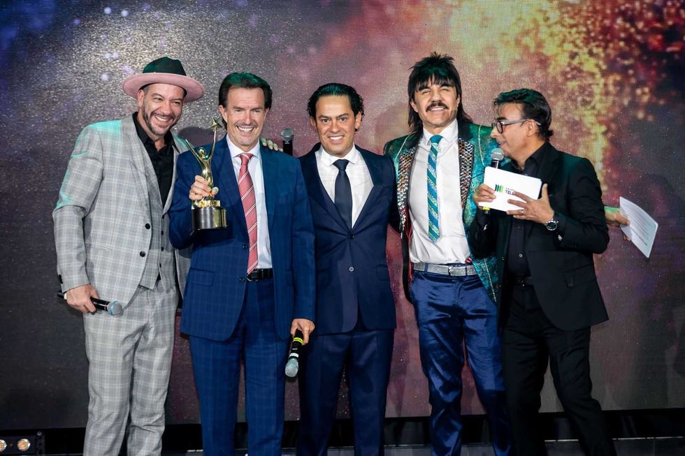 Five men in suits on stage, one holding a trophy, smiling for a photo.