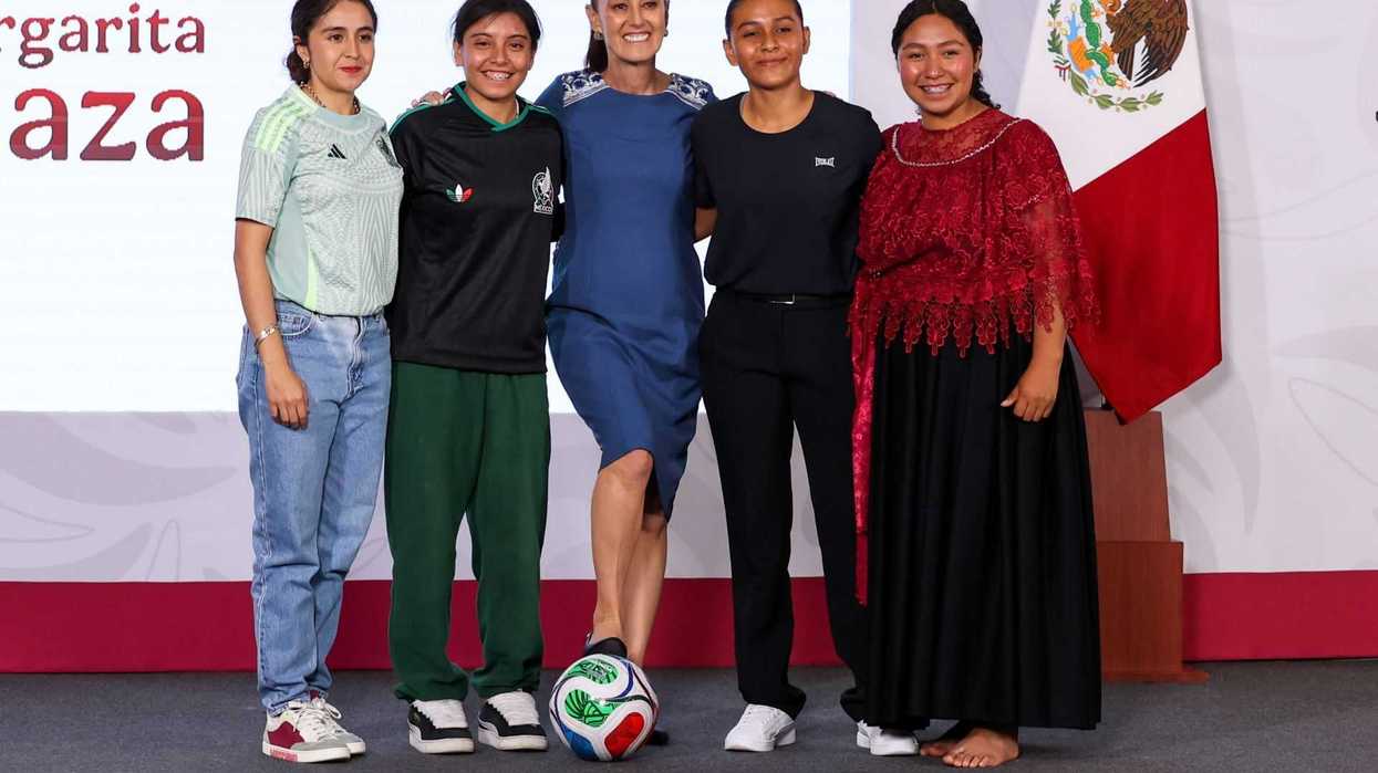 Five people smiling together on stage beside a Mexican flag and a soccer ball.