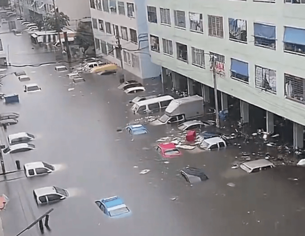 Flooded street with submerged cars beside a building.