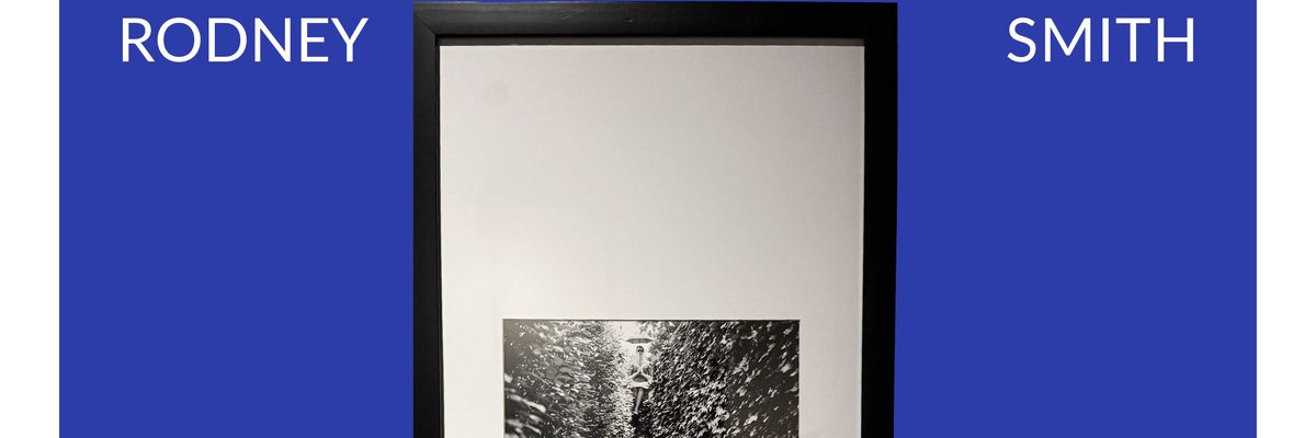 Fotografía de Rodney Smith que retrata a dos mujeres sentadas, una sostiene una lupa y la otra está al fondo sobre una barda sosteniendo un paraguas.