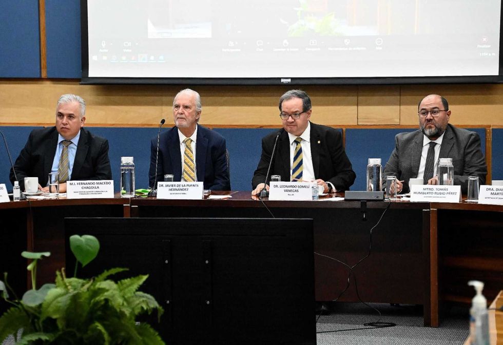 Four men in suits sitting at a conference table with microphones.