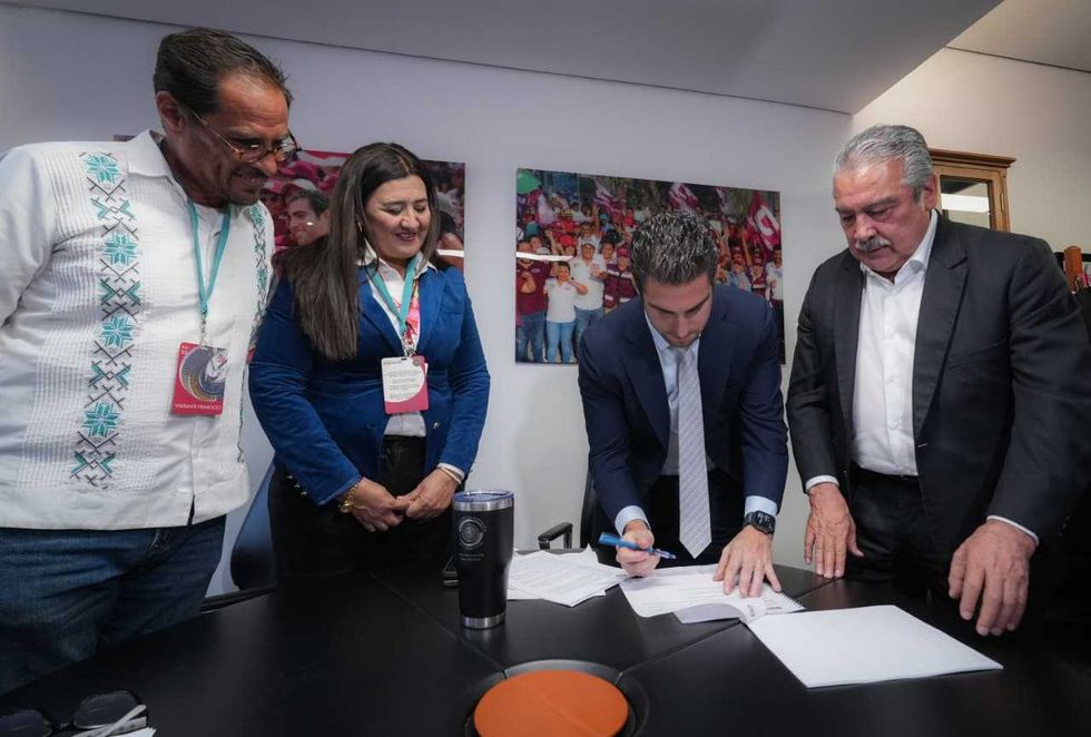 Four people gathered around a man signing a document at a table.