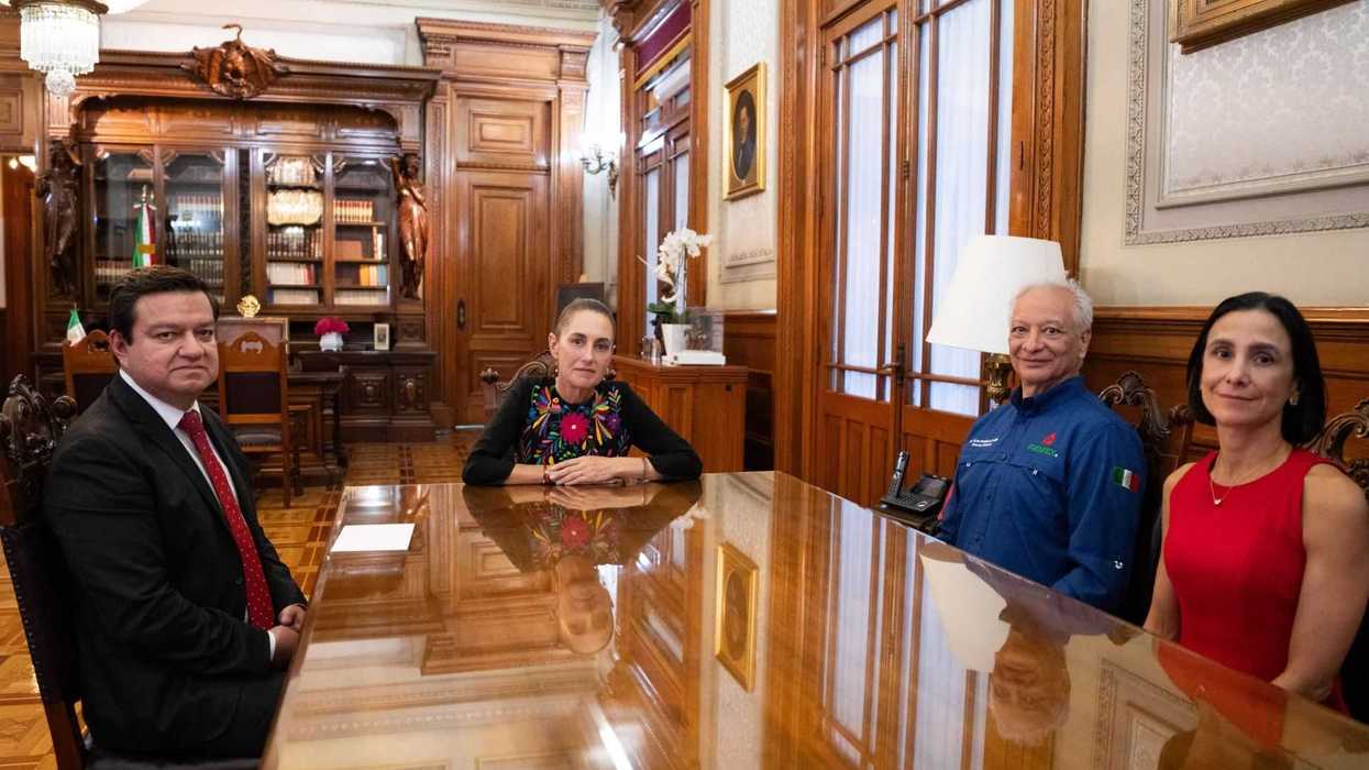 Four people seated at a polished wooden table in an ornate office setting.