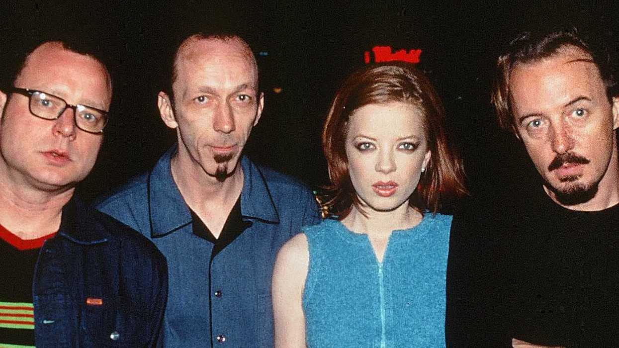 Four people standing together, facing the camera, against a dark background.
