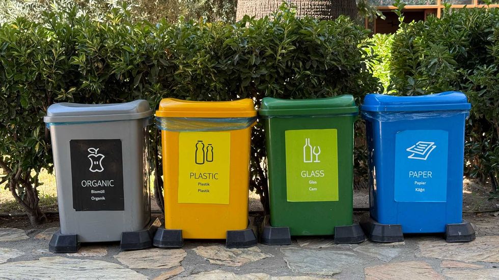 Four recycling bins: organic, plastic, glass, and paper against a hedge.