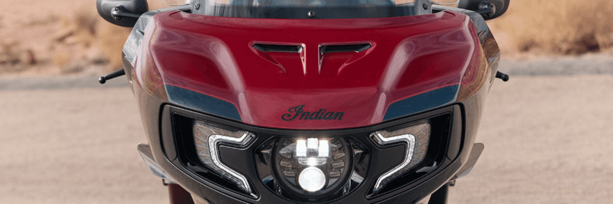 Front view of a red motorcycle with a windshield on a desert road.