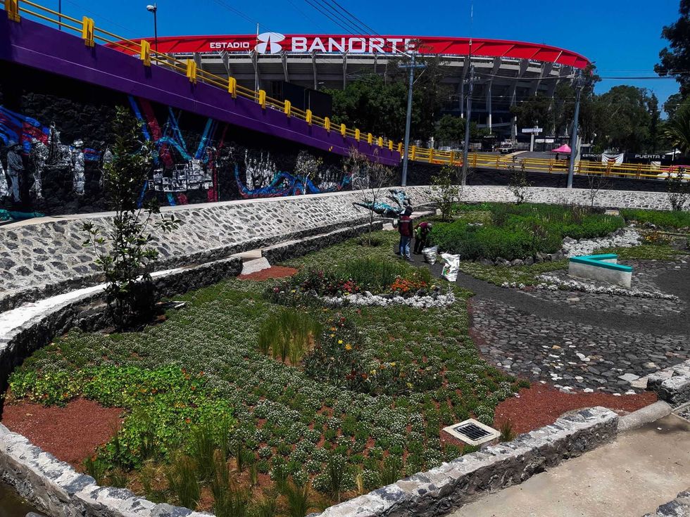Gardens near a stadium, with colorful bridge and graffiti mural in the background.