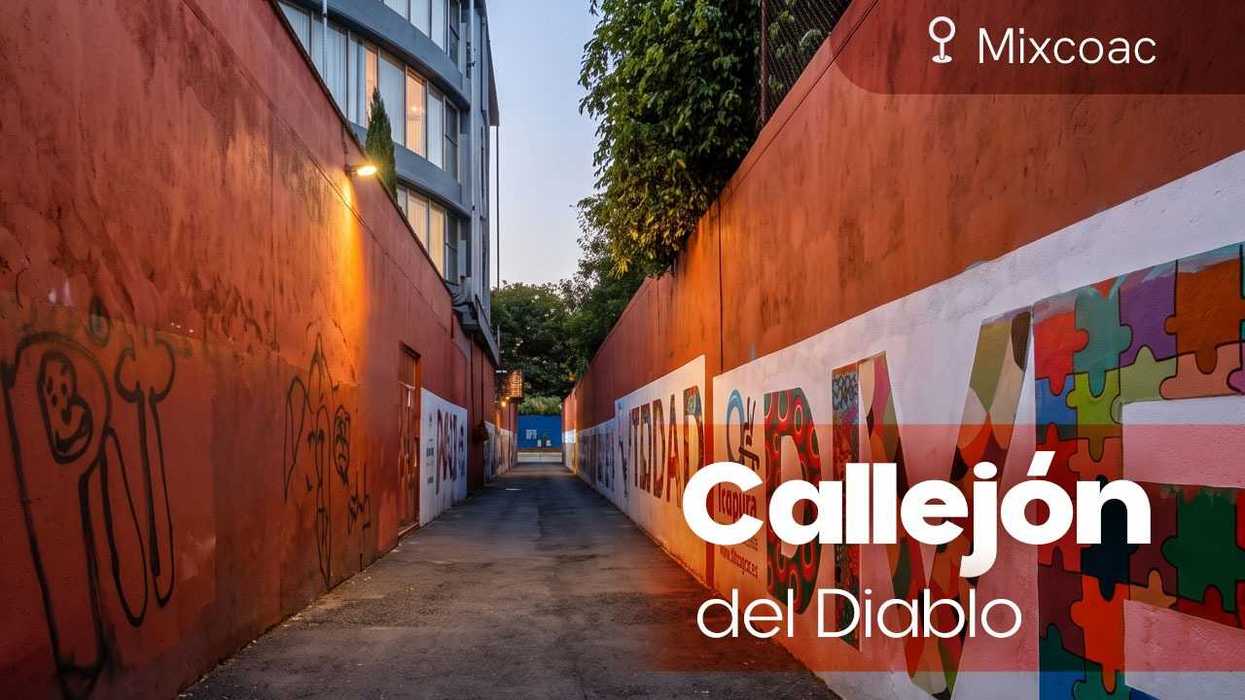 Graffiti-covered alley, "Callejón del Diablo," in Mixcoac, lit by streetlights at dusk.