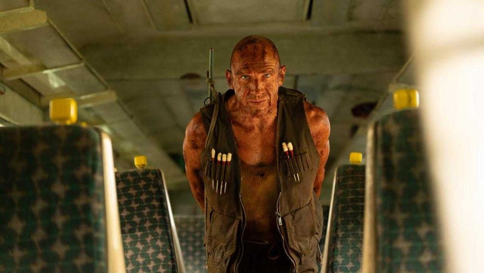 Gritty man in combat vest inside a dimly lit train, stained with dirt and focused gaze.