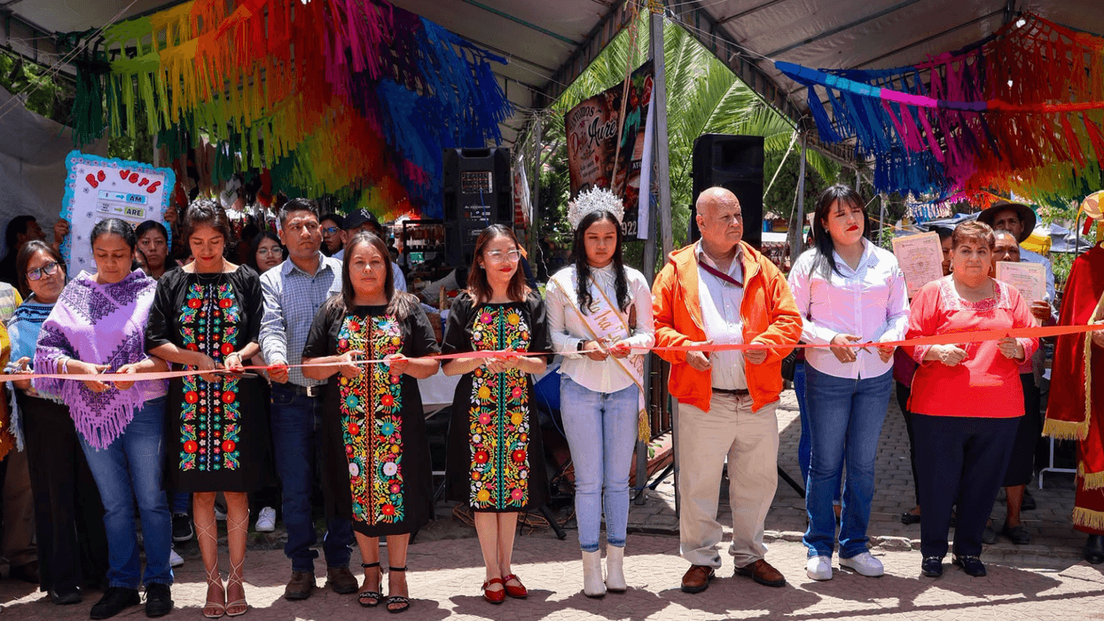 Group at ribbon-cutting ceremony under a colorful tent.