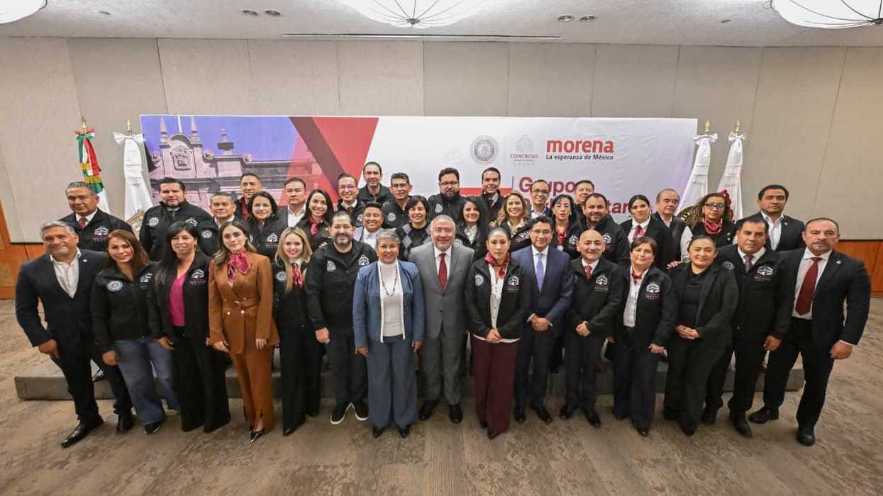 Group of people posing in front of a "Morena" banner at an indoor event.