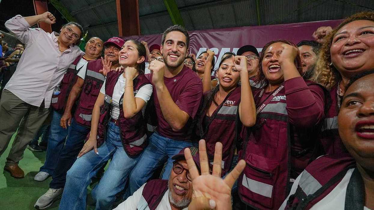 Group of people wearing maroon vests, smiling and cheering enthusiastically indoors.