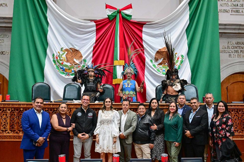 Group poses with Mexican flag backdrop; two in traditional Aztec attire.