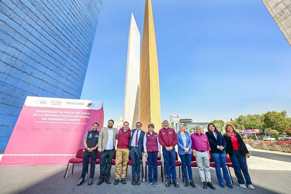 Group standing in front of colorful towers at a public event with a pink banner.
