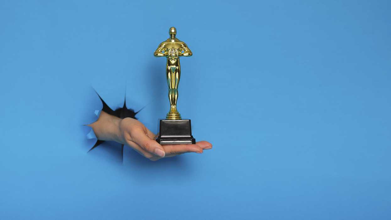Hand holding a golden trophy through a torn blue paper background.