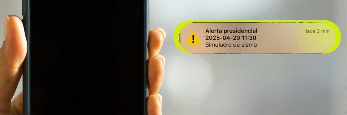 Hand holding phone with a presidential earthquake drill alert notification in Spanish.