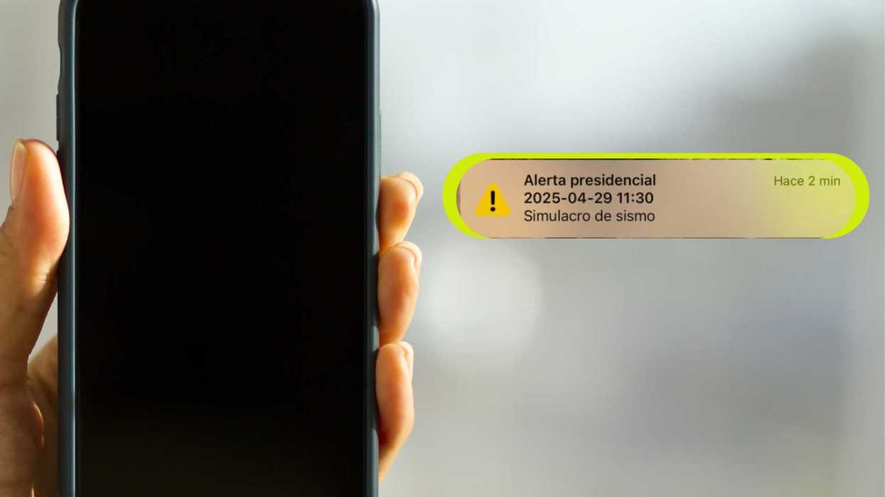 Hand holding phone with a presidential earthquake drill alert notification in Spanish.