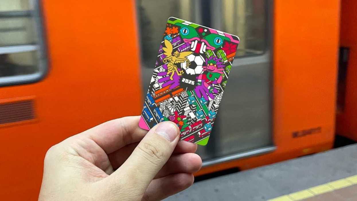 Hand holds colorful card in a subway station with an orange train in the background.