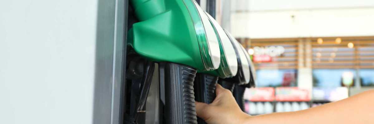 Hand reaching for a green fuel nozzle at a gas station pump.