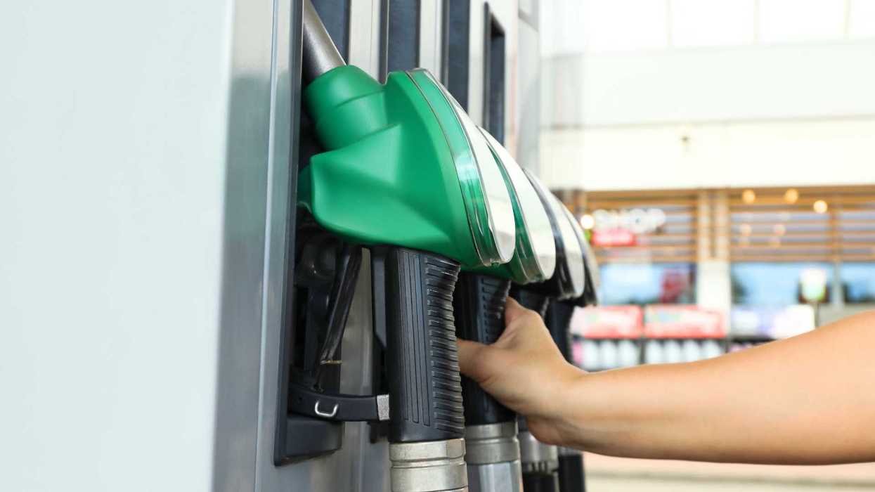 Hand reaching for a green fuel nozzle at a gas station pump.