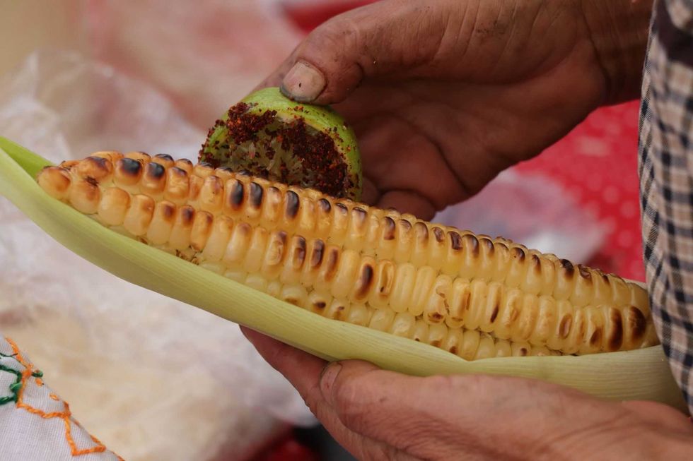 Hands seasoning grilled corn with chili-lime.