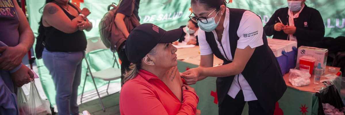 Healthcare worker administering a vaccine to a seated woman at a public health booth.