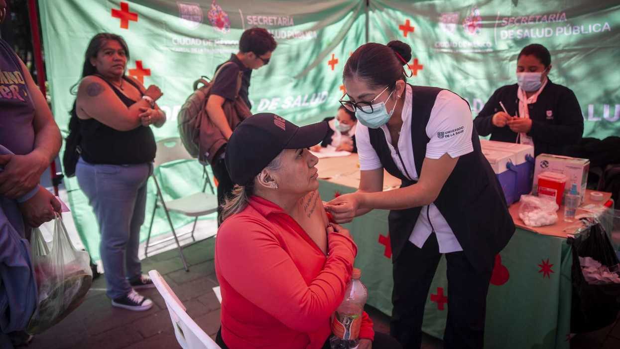 Healthcare worker administering a vaccine to a seated woman at a public health booth.