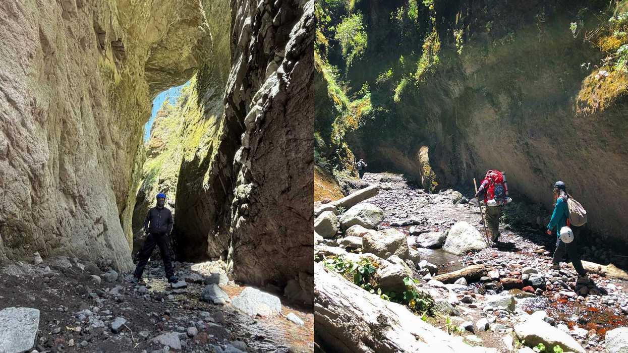Hikers explore a rocky canyon with towering, sunlit cliffs and a shallow stream.
