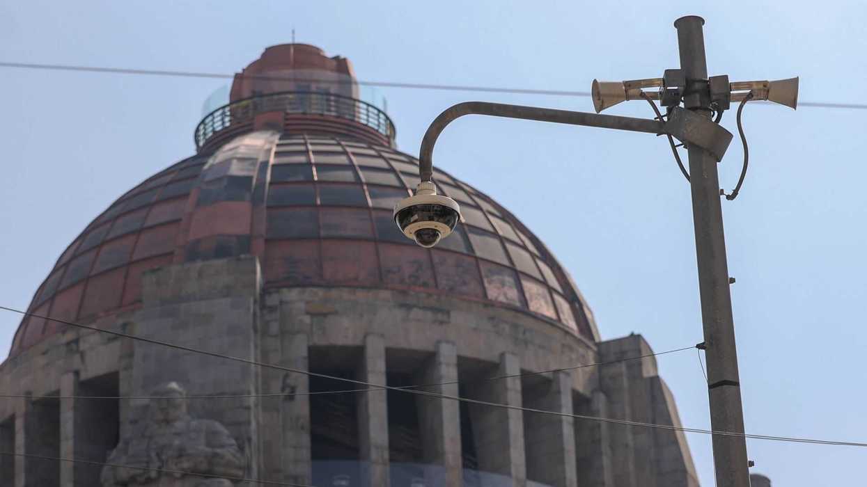 Historic dome behind a street lamp with speakers and a security camera.