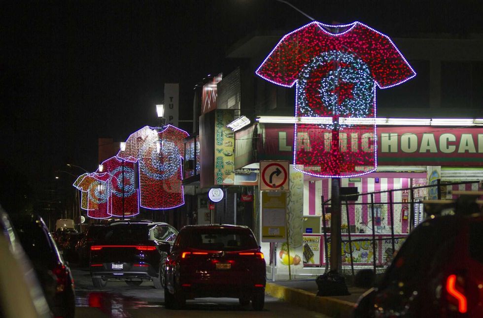 Illuminated T-shirt designs hang above a busy street at night.