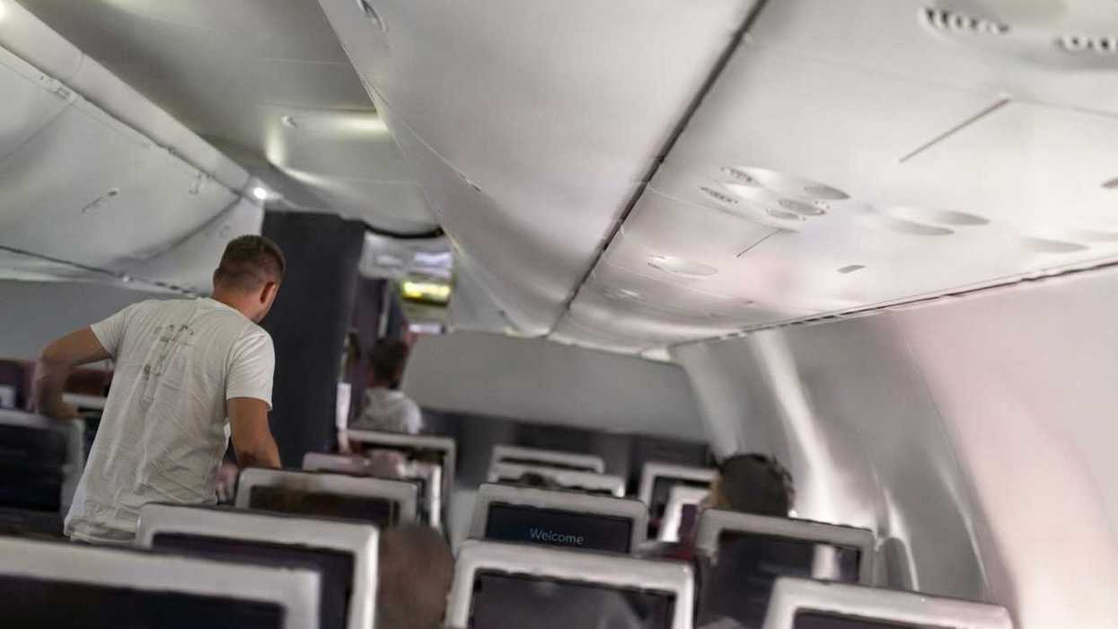 Inside an airplane cabin, passengers seated with overhead compartments closed.