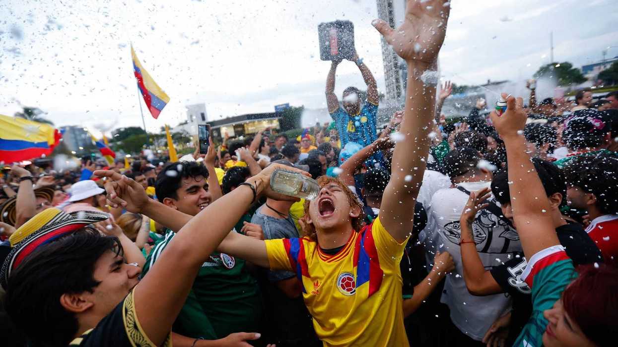 Joyful crowd celebrating with flags and foam outdoors.