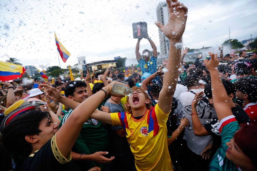 Joyful crowd celebrating with flags and foam outdoors.
