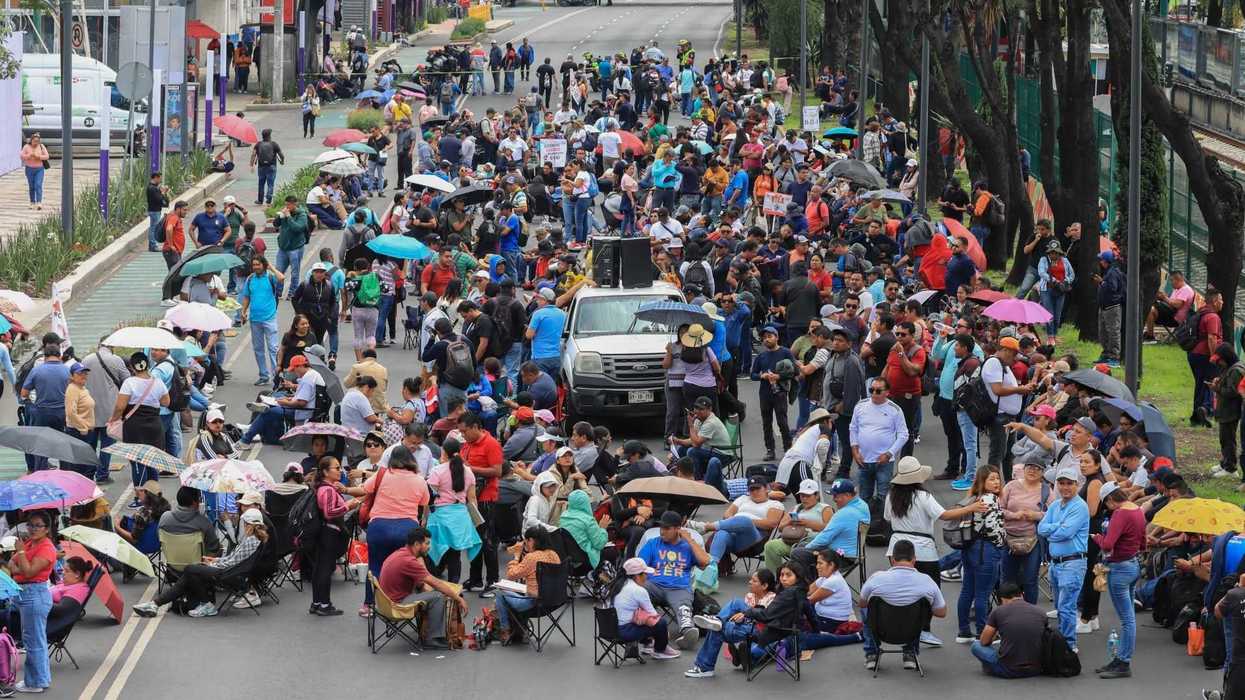 Large crowd protesting, blocking a street with umbrellas and signs.