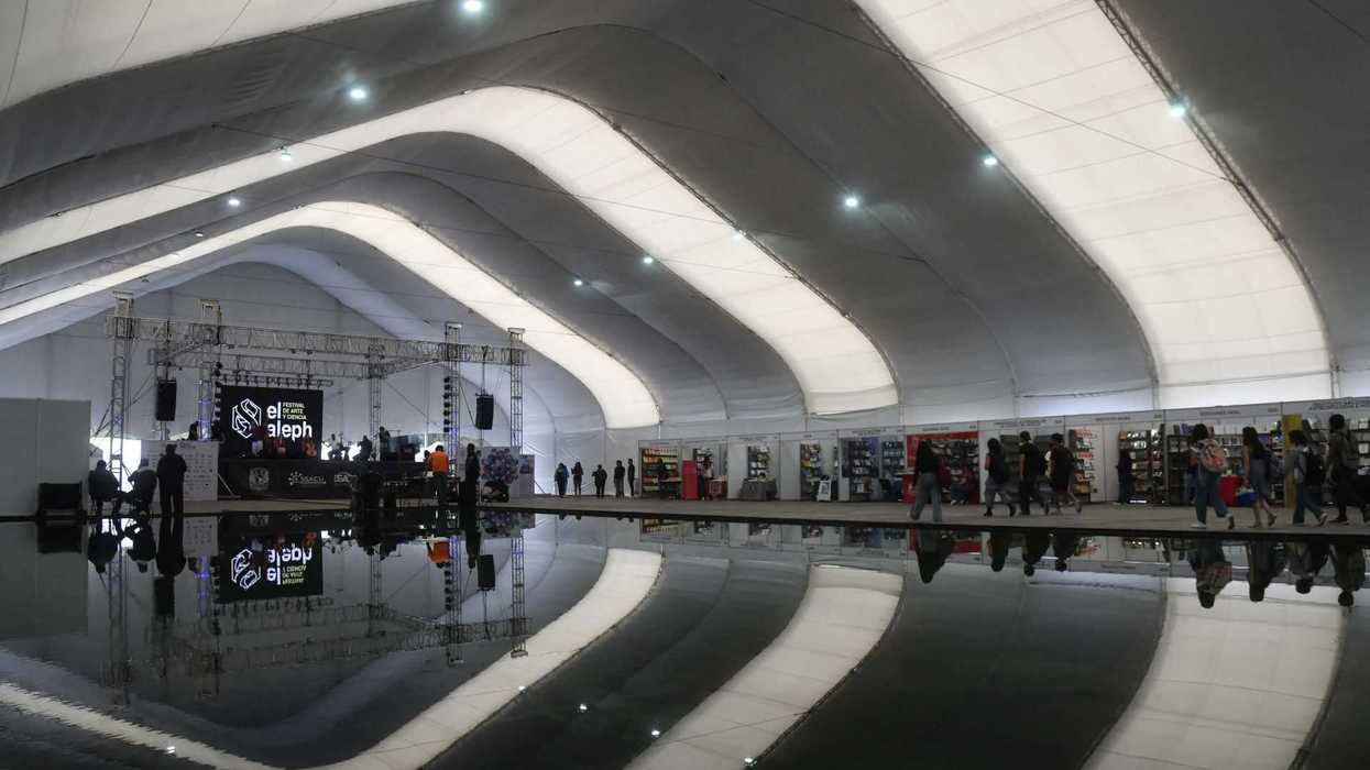 Large indoor event with arching ceiling and stage reflected in water.