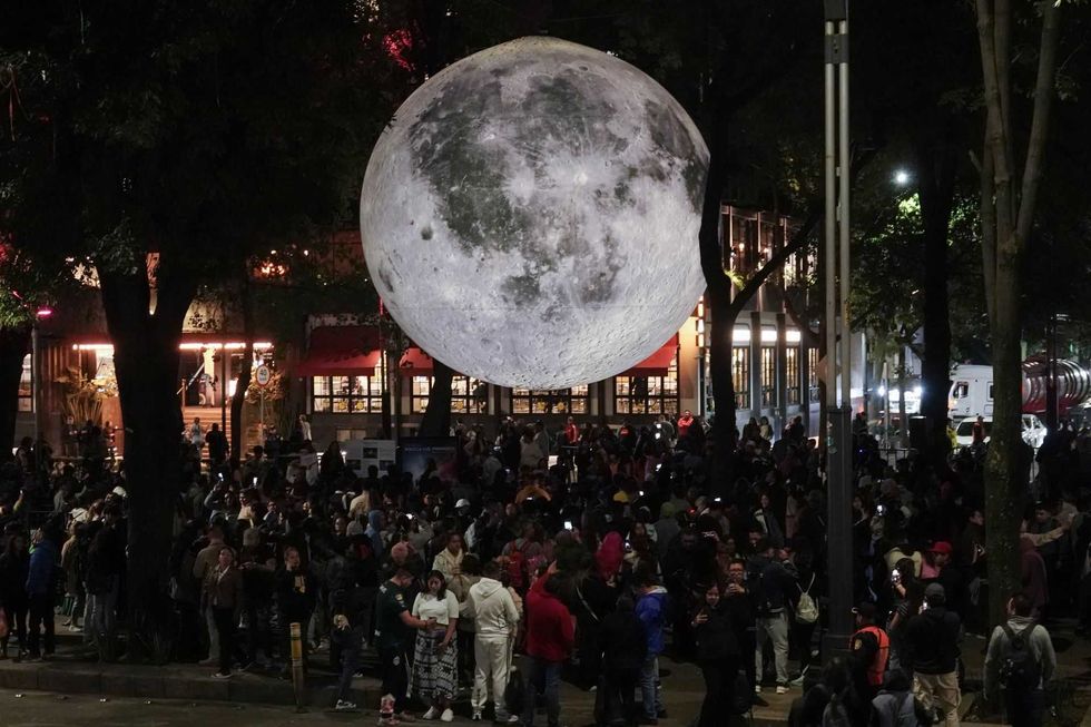Large moon replica above a bustling crowd at night in a festival setting.